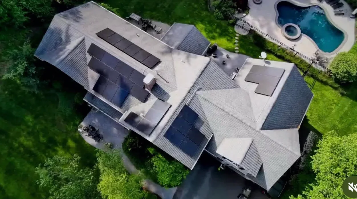 Aerial view of residential home with new gray shingle roofing, solar panels, and backyard pool