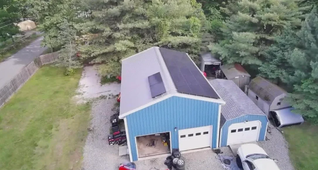 Aerial view of blue metal garage with solar panels and dual doors in wooded residential area