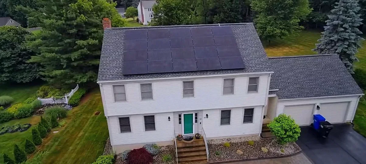 Aerial view of white colonial home with solar panel array on roof in Granby