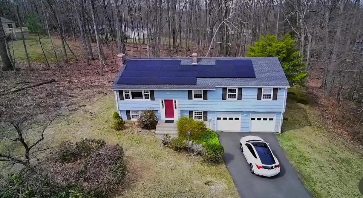 Solar panels installed on blue-roofed colonial home in wooded setting